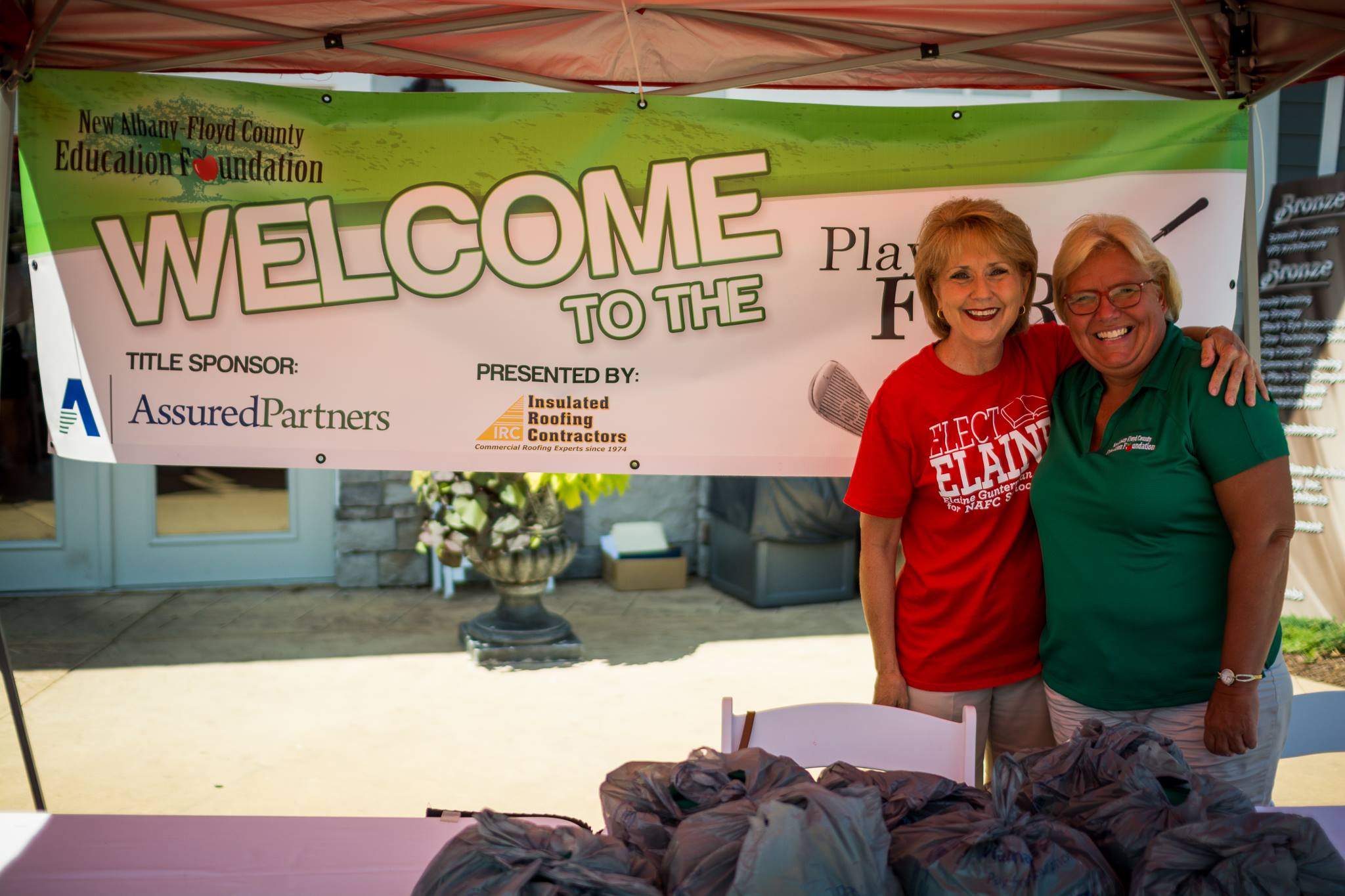 Two women standing in front of a sign that reads "Welcome to the Play Fore Education"