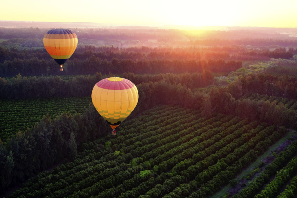 Two hot air balloons flying over countryside at sunrise.